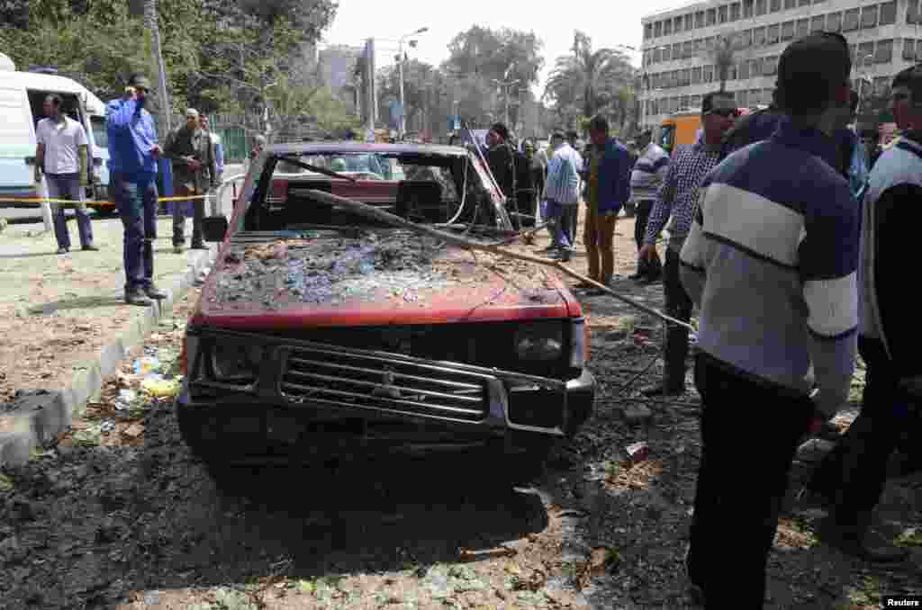 People stand near a damaged car after explosions near Cairo University, April 2, 2014. 