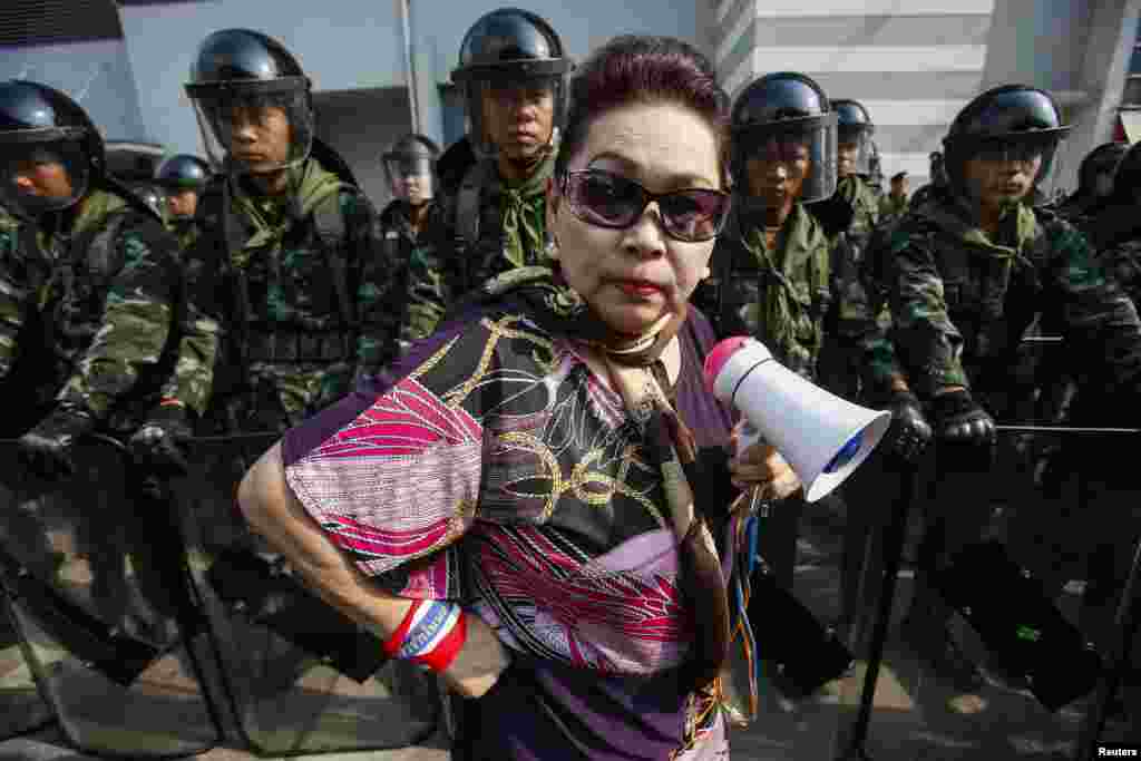 An anti-government protester stands near Thai soldiers guarding the Defence Ministry compound, which is serving as a temporary office for Thai Prime Minister Yingluck Shinawatra, in north Bangkok,