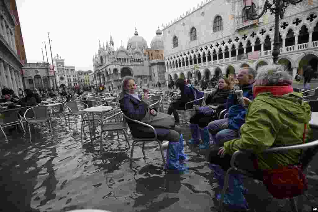 Tourists enjoy gelato as they sit in flooded St. Mark's Square in Venice, Italy.