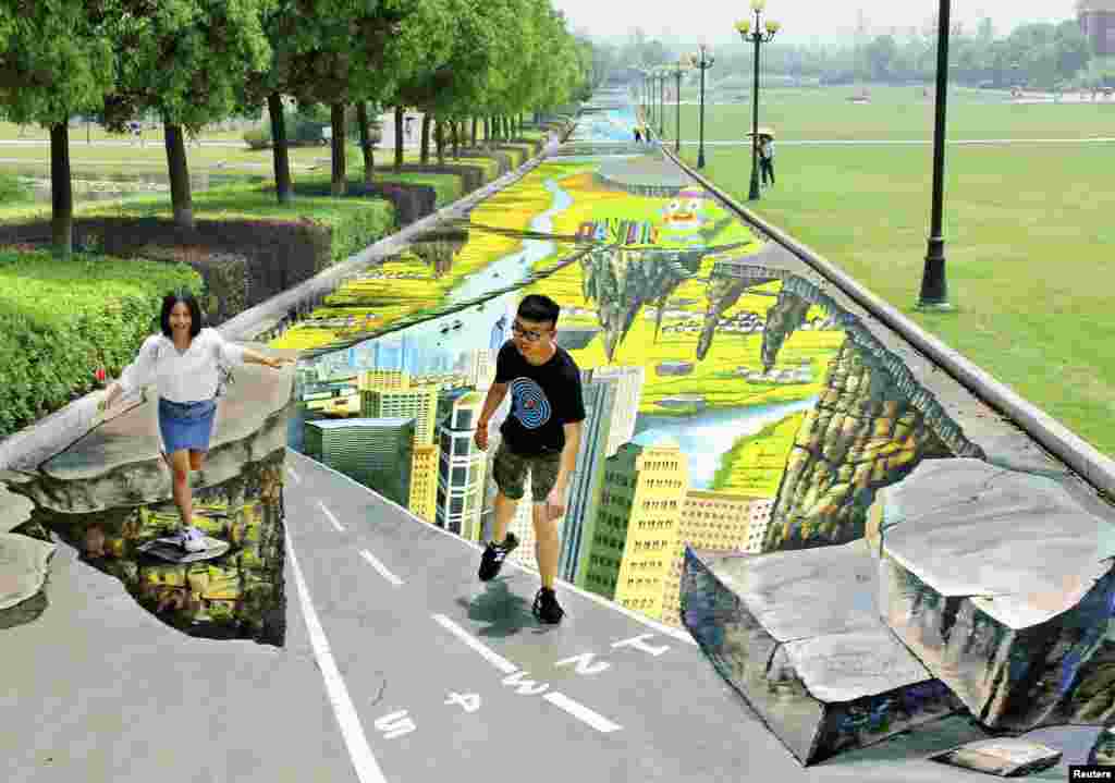 College students pose for pictures with a 3D painting along a street at a campus in Nanjing, Jiangsu province, China, June 11, 2014.