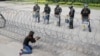 A Cambodian woman takes a photo of riot police standing behind bard wire at Freedom Park in Phnom Penh, Cambodia, May 1, 2014. 