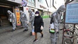 A woman wearing a face mask walks past South Korean soldiers wearing protective gear as they spray disinfectant on the street to help prevent the spread of the COVID-19 coronavirus, in Seoul on March 6, 2020.