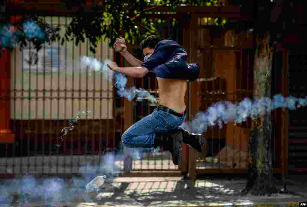 Seorang aktivis oposisi berusaha melemparkan batu ke arah pasukan keamanan yang menembakkan gas air mata, dalam aksi protes menentang Presiden Nicolas Maduro di Caracas, Venezuela.