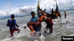 Smoke is seen on Myanmar's side of border as an exhausted Rohingya refugee woman is carried to the shore after crossing the Bangladesh-Myanmar border by boat through the Bay of Bengal, in Shah Porir Dwip, Bangladesh September 11, 2017.