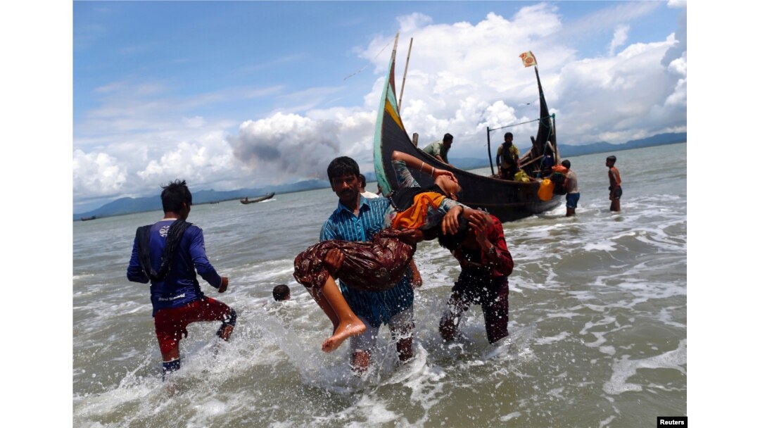 Smoke is seen on Myanmar's side of border as an exhausted Rohingya refugee woman is carried to the shore after crossing the Bangladesh-Myanmar border by boat through the Bay of Bengal, in Shah Porir Dwip, Bangladesh September 11, 2017.