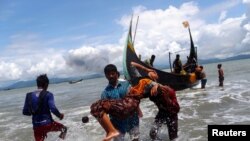 FILE - Smoke is seen on Myanmar's side of border as an exhausted Rohingya refugee woman is carried to the shore after crossing the Bangladesh-Myanmar border by boat through the Bay of Bengal, in Shah Porir Dwip, Bangladesh Sept. 11, 2017.