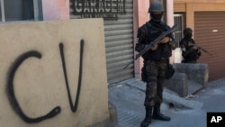FILE - A soldier stands guard next to a wall tagged with the acronym "CV" identifying the criminal organization "Comando Vermelho" or Red Command, during an operation at the Rocinha slum, in Rio de Janeiro, Brazil, Oct. 10, 2017. 
