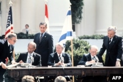 Presiden Mesir Anwar al-Sadat (kiri) dan Perdana Menteri Israel Menachem Begin (kanan) mengapit Presiden AS Jimmy Carter untuk menandatangani Perjanjian Camp David yang bersejarah, 26 Maret 1979 di Gedung Putih, Washington. Dalam perjanjian yang dimediasi AS, Israel dan Mesir sepakat menjalin perdamaian dan keamana bagi masyarakat Timur Tengah.