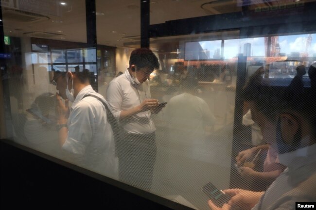Orang-orang memeriksa ponsel mereka di ruang merokok di Stasiun Shinagawa di tengah pandemi COVID-19 di Tokyo, Jepang, 2 Agustus 2021.