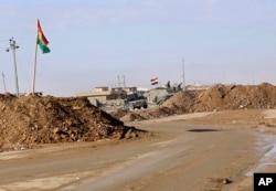 FILE - In this Dec. 3, 2016 photo, military vehicles guard an Iraqi Army checkpoint flying an Iraqi flag, center, next to a Kurdish checkpoint with a Kurdish flag, outside Irbil, northern Iraq.