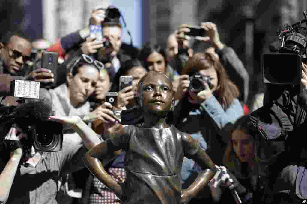 People stop to photograph the &quot;Fearless Girl&quot; statue in New York. The statue was installed by investment firm State Street Global Advisors. An inscription at the base reads, &quot;Know the power of women in leadership. She makes a difference.&quot;