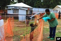 FILE - A health worker, right, feeds a boy suspected of having the Ebola virus at an Ebola treatment center in Beni, eastern Democratic Republic of Congo, Sept. 9, 2018.