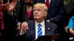 FILE - In this March 27, 2017, photo, President Donald Trump holds up a pen he used to sign one of various bills in the Roosevelt Room of the White House in Washington.
