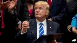 FILE - President Donald Trump holds up a pen he used to sign one of various bills in the the White House in Washington, March 27, 2017. Leaders across the U.S. are vowing to fight against Trump's crackdown on "sanctuary cities."