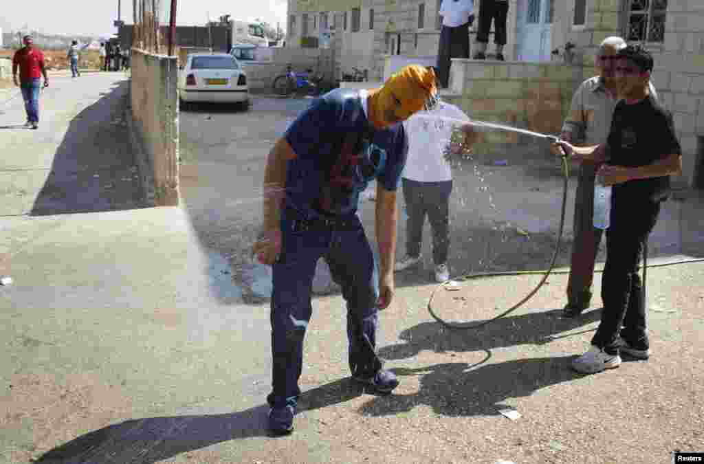 A masked Palestinian youth is hosed down with water to cool down from the afternoon heat at the funeral of 16-year-old Mohammed Abu Khudair in Shuafat, an Arab suburb of Jerusalem, July 4, 2014.