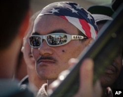 FILE – Sunglasses worn by an Americans gang member reflect the scene of a drug raid in Valhalla Park, a neighborhood in Cape Town, South Africa, Aug. 14, 1996. The notorious gang has been entrenched for decades. (AP) Click on photo for related video.