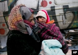 A migrant mother holds her baby walking towards a passenger train in Presevo, close to the Serbian border with Macedonia, 300 kilometers southeast of Belgrade, Serbia, Jan. 18, 2016.