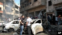 Warga berkumpul di lokasi ledakan dua bom yang meledak di distrik Zahra, Homs (29/4). (AP/SANA)