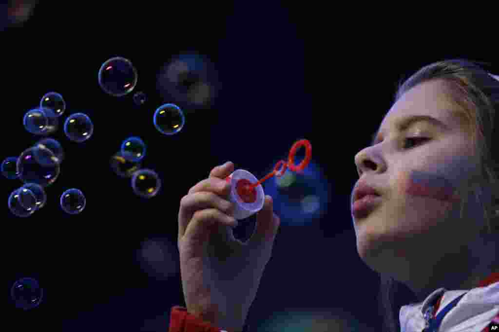 A girl, the Russian flag painted on her face, blows bubbles as she waits for the start of the closing ceremony of the 2014 Winter Olympics in Sochi, Feb. 23, 2014.