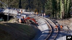 In this photo from Dec. 20, 2017, people work at the curve leading to the railroad bridge where an Amtrak train derailed onto Interstate 5 two days earlier at DuPont, Wash.