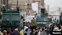 FILE - A follower of the Shi'ite Houthi movement waves the movement's flag as he stands in front of riot police vehicles along a main road leading to the airport in Sanaa, September 7, 2014.