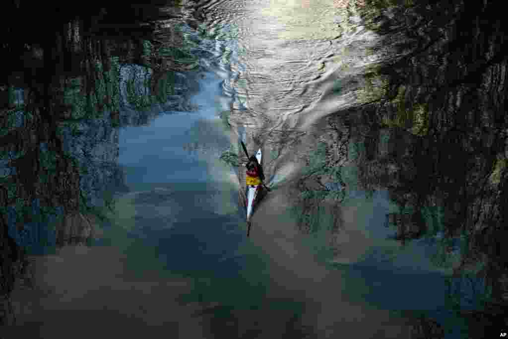 Bayangan pohon-pohon terlihat di sungai Arga sementara seorang mengayuh kayaknya di Pamplona, Spanyol utara.