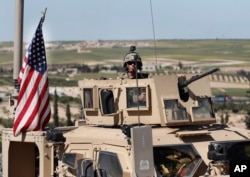 FILE - A U.S. soldier sits atop an armored vehicle, in Manbij, Syria, April 4, 2018.