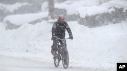 A man rides on his bicycle as fresh snow falls, Dec. 29, 2017, in Erie, Pa.