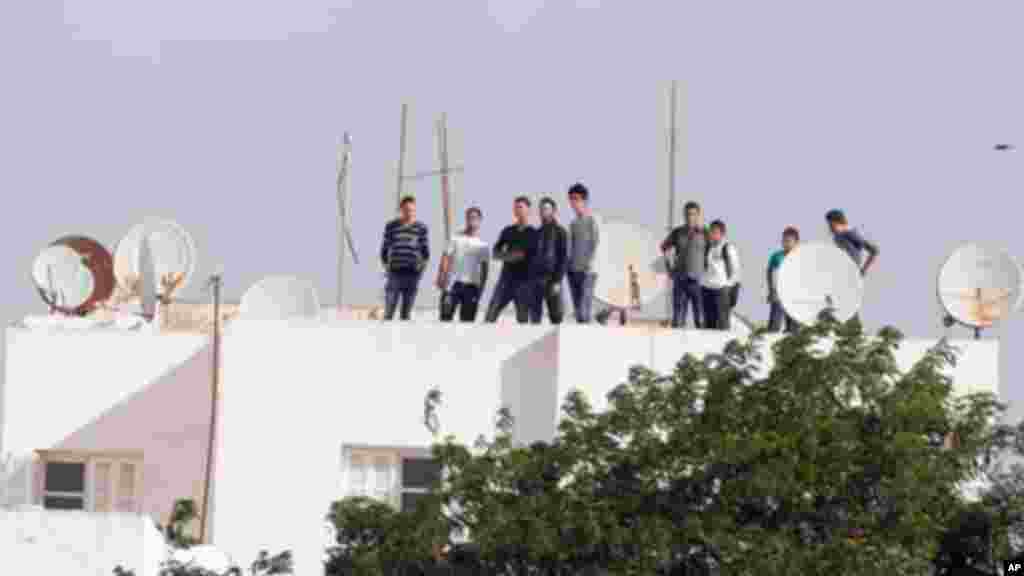 Des jeunes tunisiens, debout sur un toit, regardent les opérations policières en cours après une fusillade avec des militants dans la banlieue Oued Ellil de Tunis, Tunisie, le jeudi 23 octobre 2014. Un agent de sécurité a été tué dans lae fusillade. (AP Photo/Aimen Zine) 