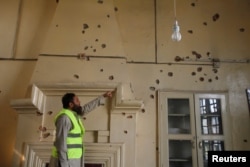 A rescue worker points to bullet holes in the wall of a computer lab after the shooting at Directorate of Agriculture Institute in Peshawar, Pakistan, Dec. 1, 2017.