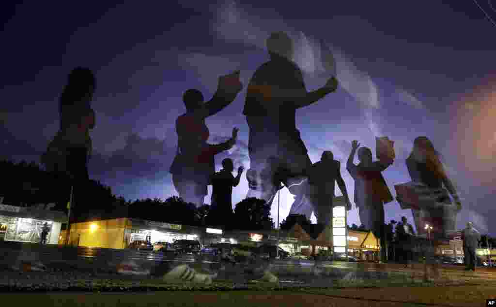 Protesters march in the street as lightning flashes in the distance in Ferguson, Mo., Aug. 20, 2014.