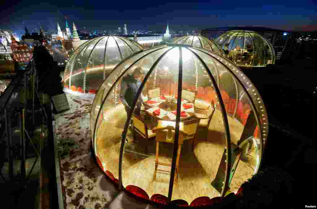 A waiter sets a table inside a transparent pod offered for private Christmas meals with backdrop of the Kremlin and Red Square on the rooftop of Ritz-Carlton hotel in Moscow, Russia, Dec. 8, 2020.