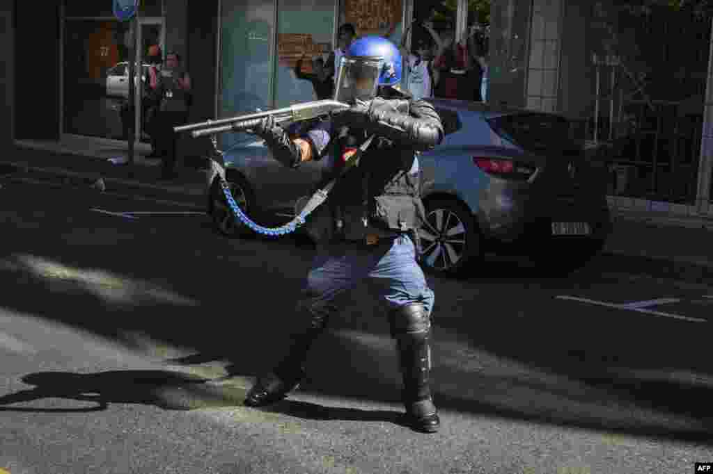 A member of the South African riot police disperses students supporting the "Fees Must Fall Movement" protest outside the South African Parliament where the South African Minster of Finance delivered his Mid-term Budget address in Cape Town.
