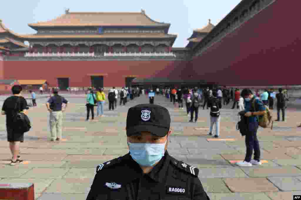 A security guard stands watch as people line up while ensuring social distancing to enter the Forbidden City, the former palace of China&#39;s emperors, in Beijing. The area was reopened three months after it closed due to the coronavirus crisis.