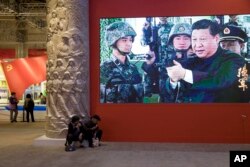 In this Oct. 19, 2017, photo, video showing Chinese President Xi Jinping handling an assault rifle is shown at an exhibition highlighting China's achievements under five years of his leadership.