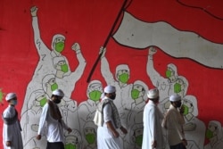 Pria Muslim berjalan melewati mural yang menampilkan orang-orang yang mengenakan masker selama pandemi COVID-19 di Jakarta pada 29 Januari 2021. (Foto: AFP/Adek Berry)