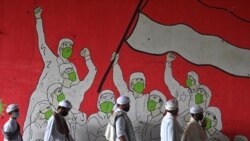 Rombongan Pria Muslim berjalan melewati mural yang menampilkan orang-orang yang mengenakan masker selama pandemi COVID-19 di Jakarta pada 29 Januari 2021. (Foto: AFP/Adek Berry)