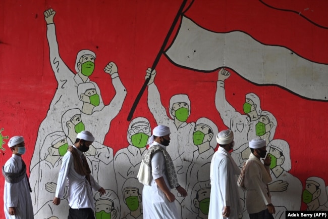 Pria Muslim berjalan melewati mural yang menampilkan orang-orang yang mengenakan masker selama pandemi COVID-19 di Jakarta pada 29 Januari 2021. (Foto: AFP/Adek Berry)