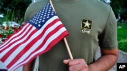 Un recluta pakistaní, de 22 años, quien recientemetne fue dado de baja del Ejército de EE.UU., sostiene una bandera estadounidense mientras posa para una fotografía, julio, 3, 2018.
