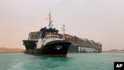 In this photo released by the Suez Canal Authority, a boat navigates in front of a cargo ship, Ever Given, Wednesday, March 24, 2021, after it become wedged across Egypt’s Suez Canal and blocked all traffic in the vital waterway. (Suez Canal Authority via AP)