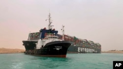 In this photo released by the Suez Canal Authority, a boat navigates in front of a cargo ship, Ever Given, Wednesday, March 24, 2021, after it become wedged across Egypt’s Suez Canal and blocked all traffic in the vital waterway. (Suez Canal Authority via