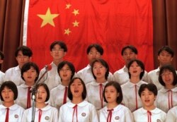 Sejumlah siswa di Hong Kong bernyanyi di depan bendera nasional China untuk merayakan Hari Kemerdekaan China. (Foto: AP)