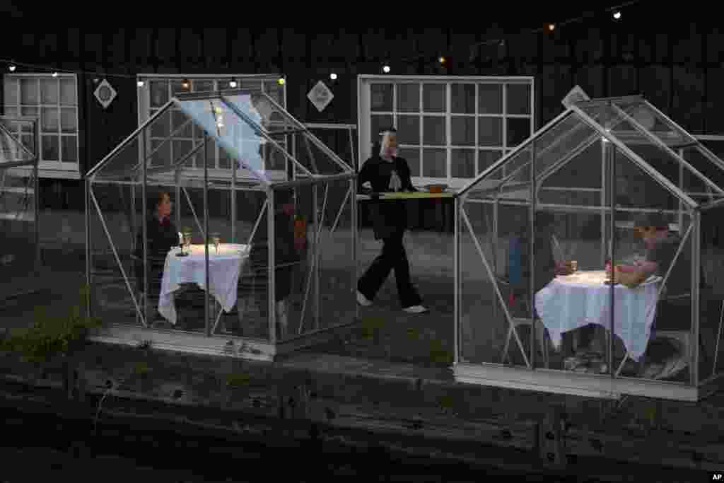 Staff at the Mediamatic restaurant serve food to volunteers seated in small glasshouses during a try-out of a setup which respects social distancing to combat the spread of the COVID-19 in Amsterdam, Netherlands, Tuesday, May 5, 2020. (AP Photo/Peter Dejo