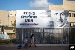 Children pass a campaign poster for Israeli Prime Minister Benjamin Netanyahu, who seeks a fourth term. The Hebrew poster says of the general election: ‘On March 17, we replace him, we replace the despair.’