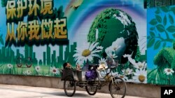 A migrant worker listens to radio on his tricycle cart parked next to a billboard promoting environment protection with the slogan "Environment protection starts from you and me" on display at the Central Business District of Beijing, June 5, 2017. 