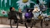 A migrant worker listens to radio on his tricycle cart parked next to a billboard promoting environment protection with the slogan "Environment protection starts from you and me" on display at the Central Business District of Beijing, June 5, 2017. 