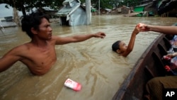 A boy receives food as a man waits near half-submerged residences in Nyaung Tone, in the Irrawaddy Delta, southwest of Yangon, Myanmar, Aug. 7, 2015. Dozens have died from recent weeks of flooding and more than hundreds of thousands have been affected.