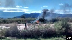 A man stands near the smoking remains of a helicopter that crashed with another near Villa Castelli in the La Rioja province of Argentina, March 9, 2015.