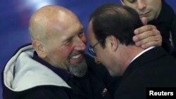 French President Francois Hollande (R) and former hostage Serge Lazarevic hug each other after delivering speeches at the Villacoublay military airport, near Paris, Dec. 10, 2014.