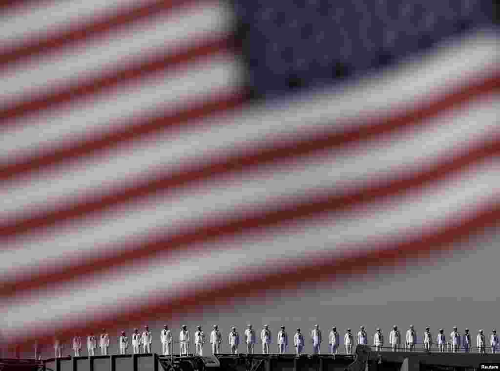 The crew members of the USS Ronald Reagan, a Nimitz-class nuclear-powered super carrier, saluting is seen behind the national flag of the U.S. as it arrives at the U.S. naval base in Yokosuka, south of Tokyo, Japan.